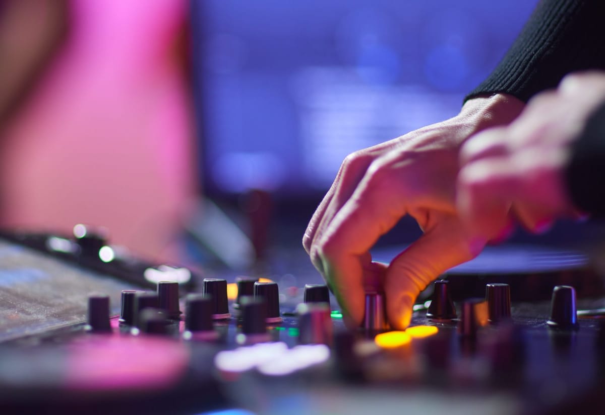 Hände an den Reglern eines DJ-Controllers im farbigen Licht eines Clubs